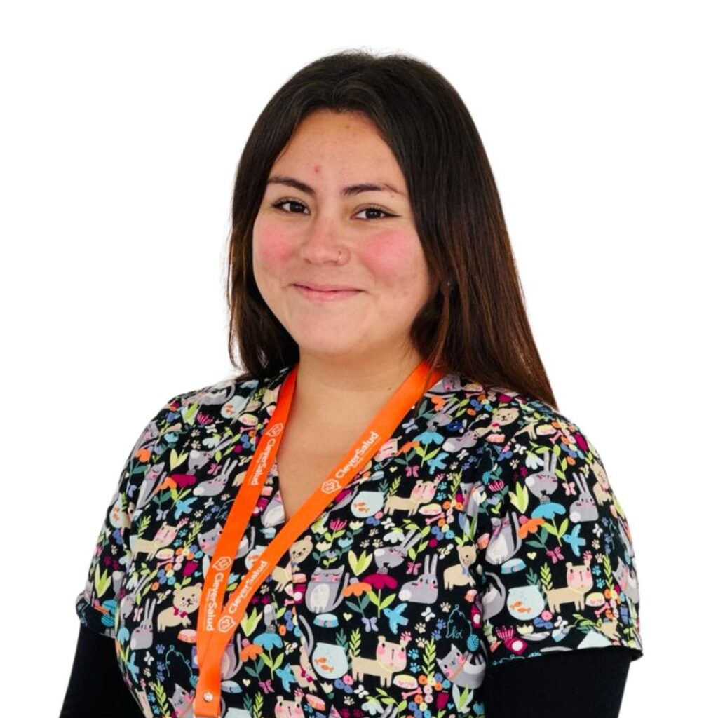 Smiling woman wearing a colorful animal-print scrub top and an orange lanyard, standing against a white background.