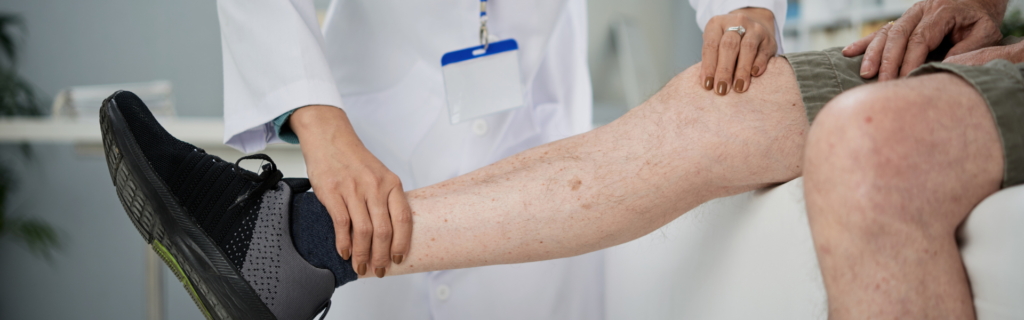 Medical professional examines a patient's leg, supporting the shin during a check-up with a blue ID badge visible on white coat.