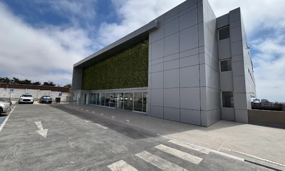 Modern gray commercial building with a vertical garden wall and glass entrance, cars parked in the foreground.