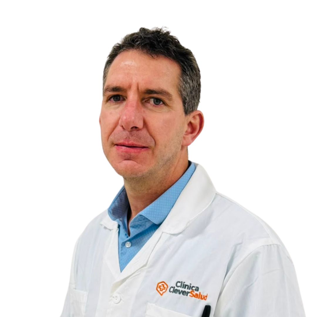 Portrait of a male doctor in a white lab coat over a blue shirt, looking at the camera, with Clinica Clever Salud logo on the coat pocket.