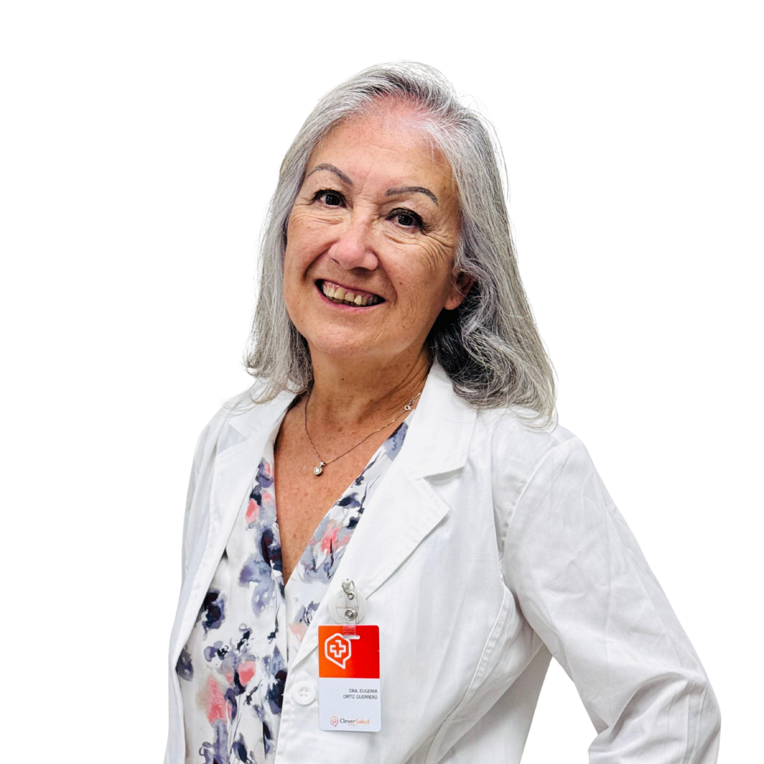 Smiling senior female doctor in a white coat with a floral blouse and ID badge, posing against a white background.