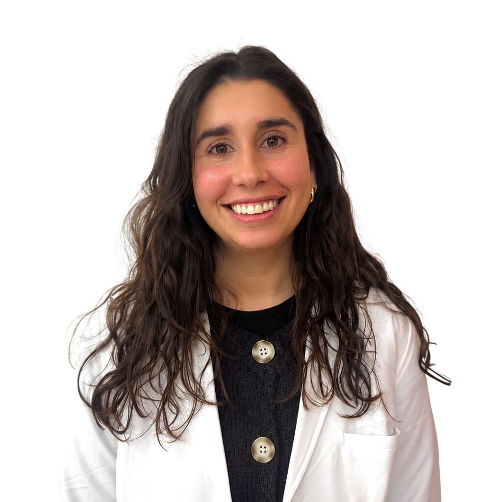Smiling young woman with long dark hair wearing a white lab coat over a black top.