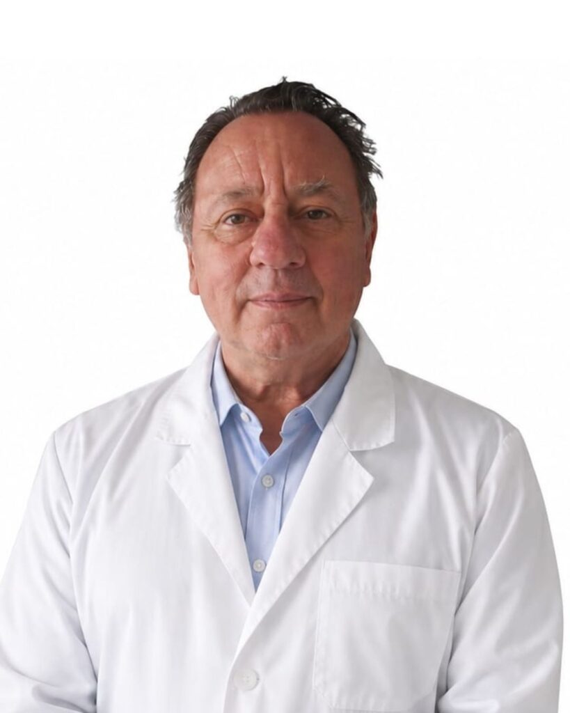 Male doctor in a white lab coat and light blue shirt, standing against a white background.