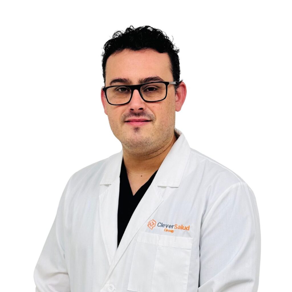 Male doctor wearing glasses and a white lab coat with Clever Salud Group branding, facing the camera.