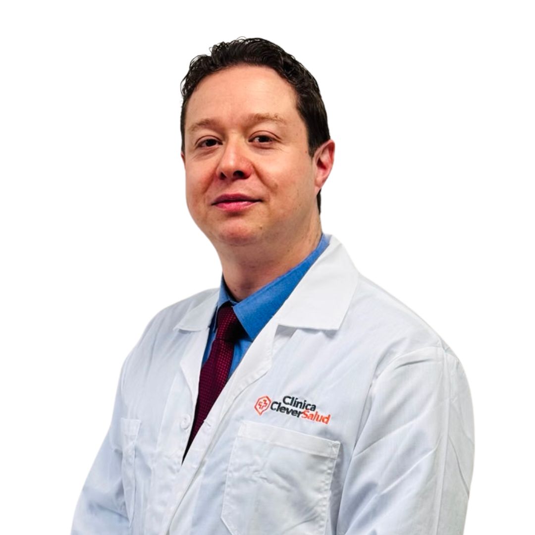 Portrait of a male doctor in a white coat with a blue shirt and red tie, standing against a white background, logo visible on coat pocket.