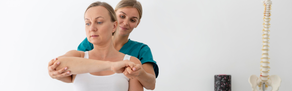 Therapist guides a patient through a shoulder stretch during physical therapy in a clinic, with a spine model visible in the background.