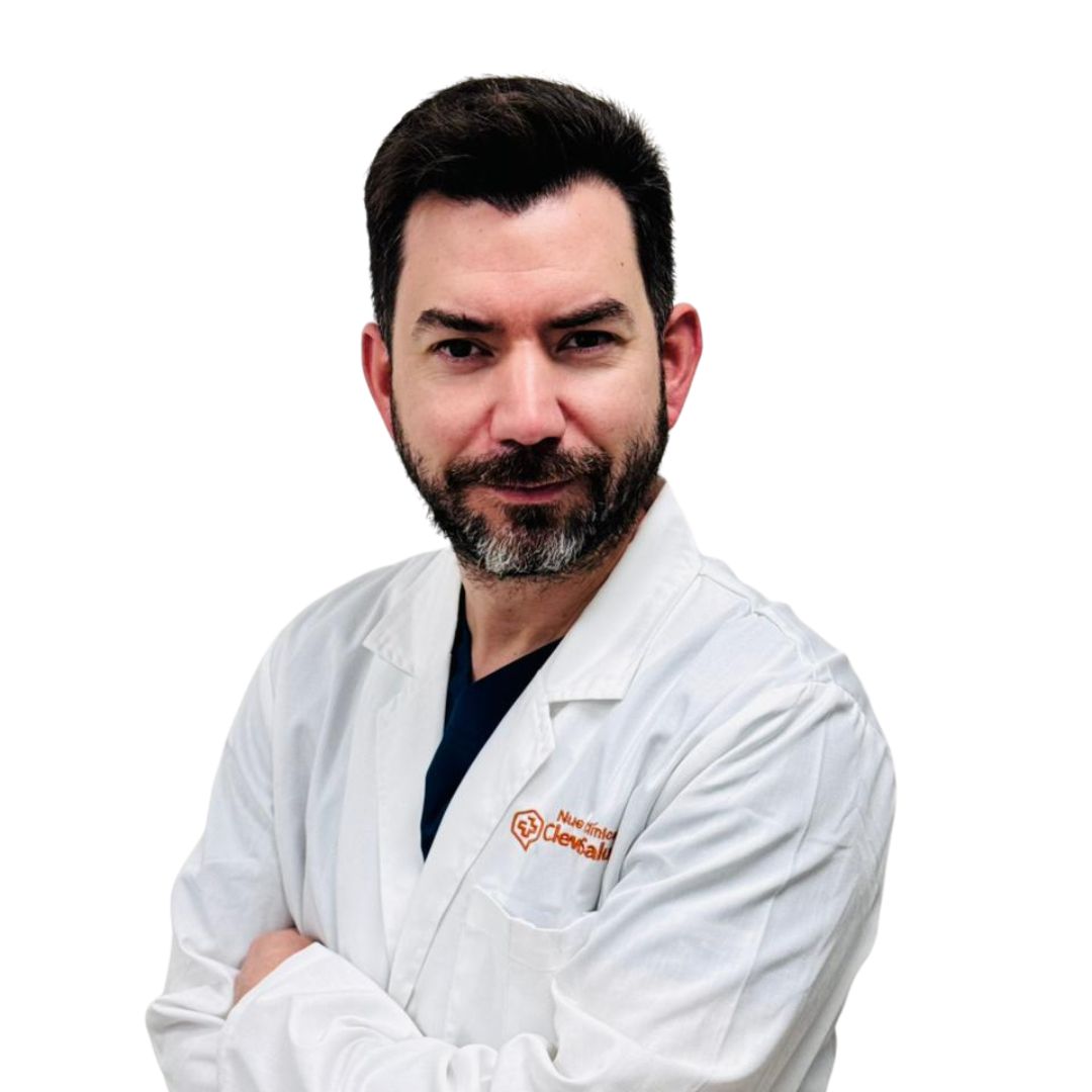 Male doctor with dark hair and beard in a white lab coat, arms crossed, looking at the camera.