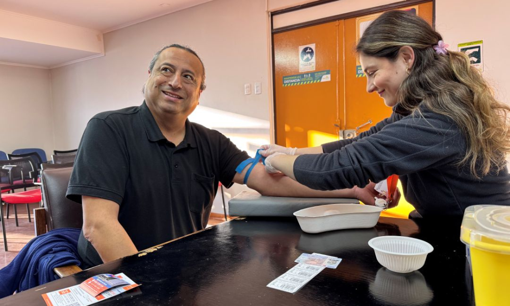 Man seated at a table as a nurse draws his blood for donation, in a bright clinic room.]','
