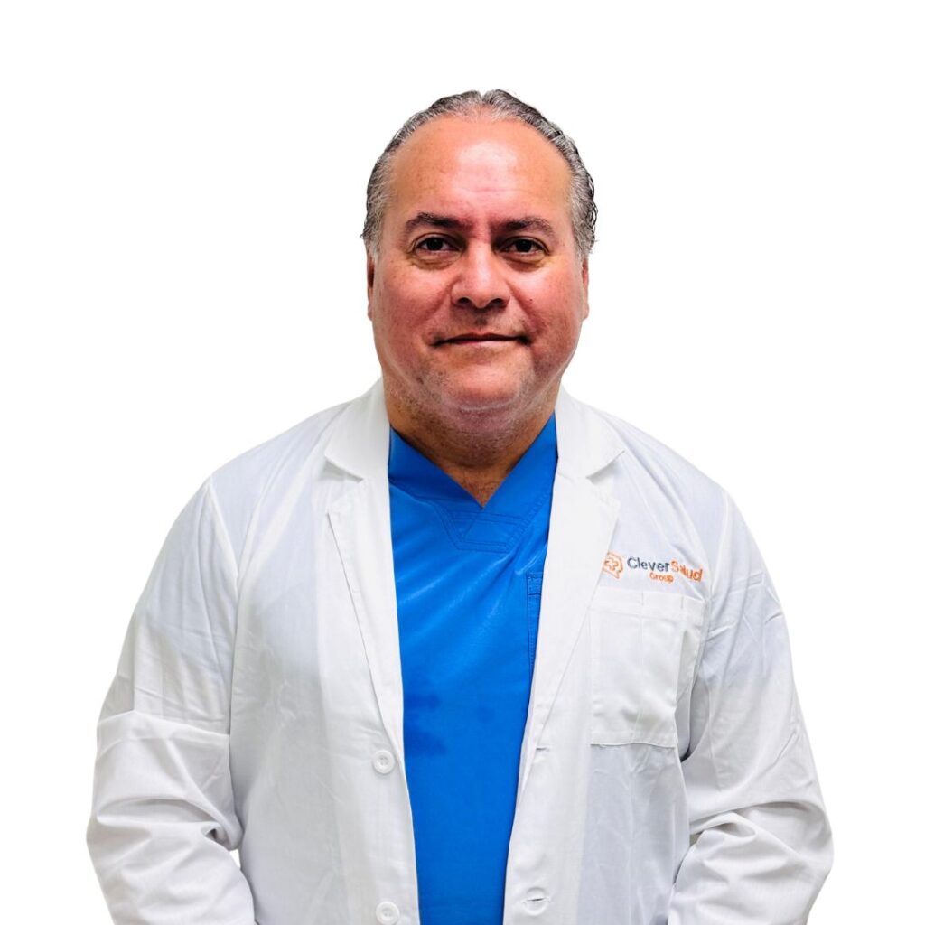 Smiling male doctor in a white lab coat over blue scrubs, posing against a white background.