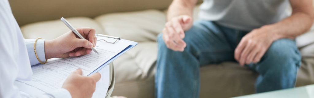 Clinician writing on a clipboard during a patient consultation on a sofa.