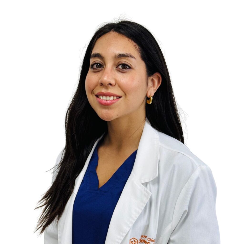 Smiling female doctor or healthcare professional with long dark hair, wearing a white coat over blue scrubs.