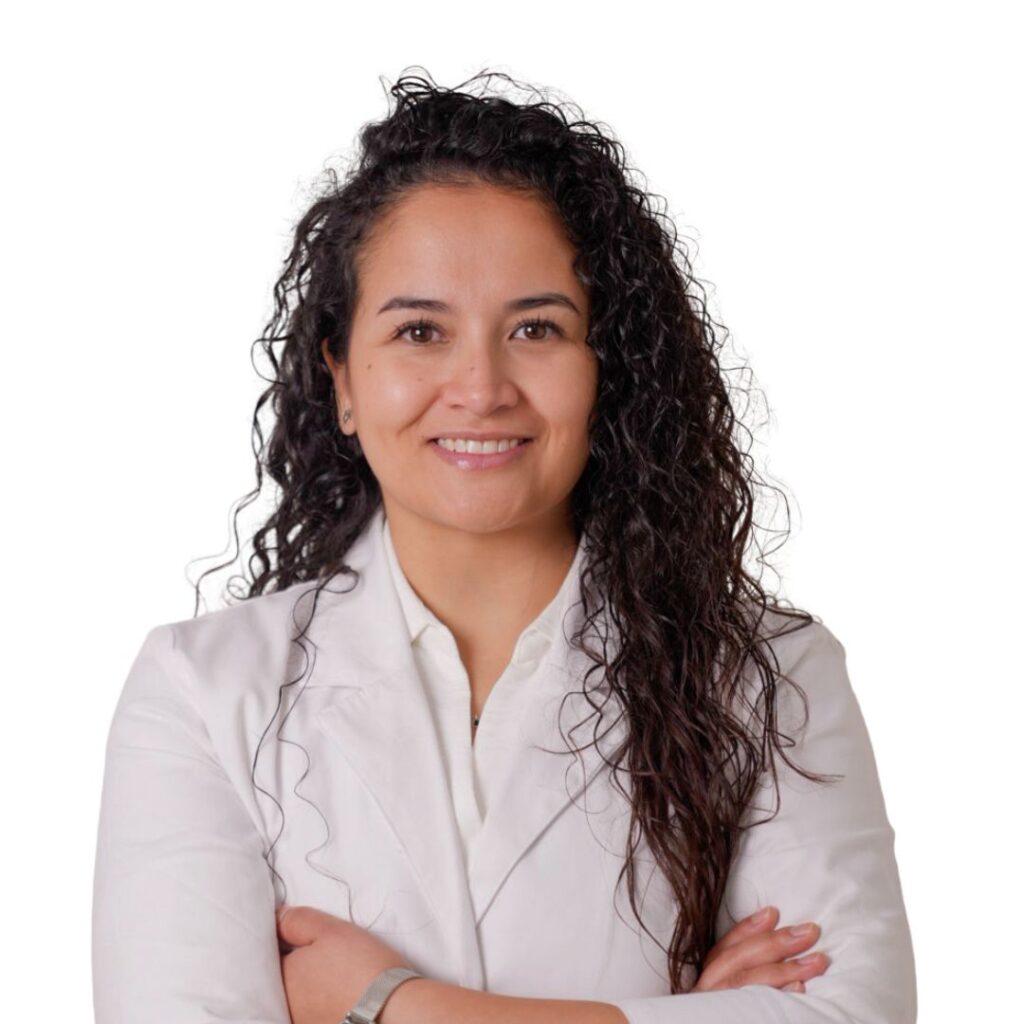 Professional portrait of a smiling woman with curly black hair, wearing a light blazer and arms crossed against a white background.